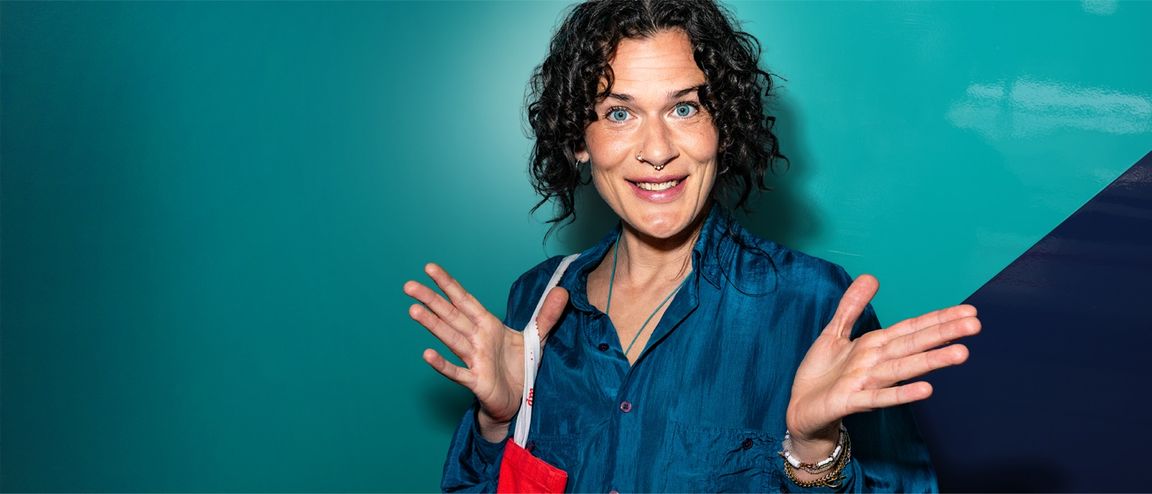 Frau mit lockigem Haar und blauer Bluse vor türkisfarbenem Hintergrund