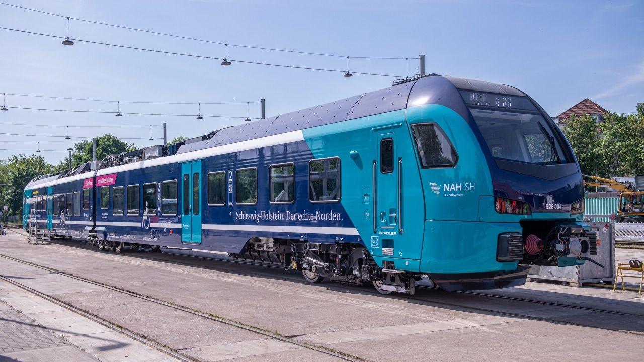 Türkisfarbener NAH.SH-Zug an einem Bahnsteig im Sonnenlicht